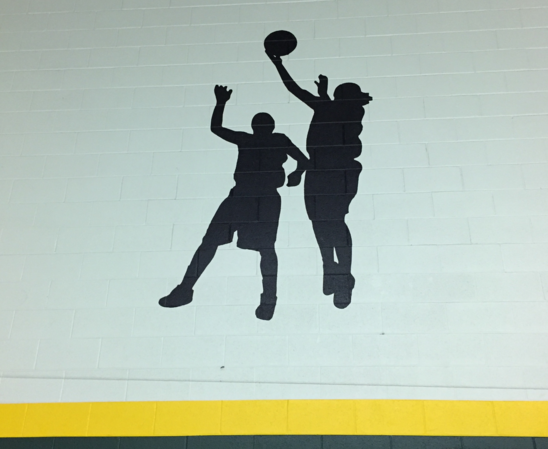 Silhouettes of 2 students leaping for a basketball.